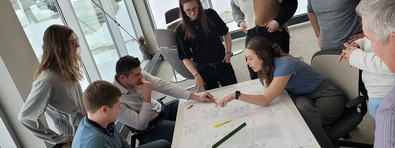 A group of Shive-Hattery employees work together around a table with charts and diagrams on it