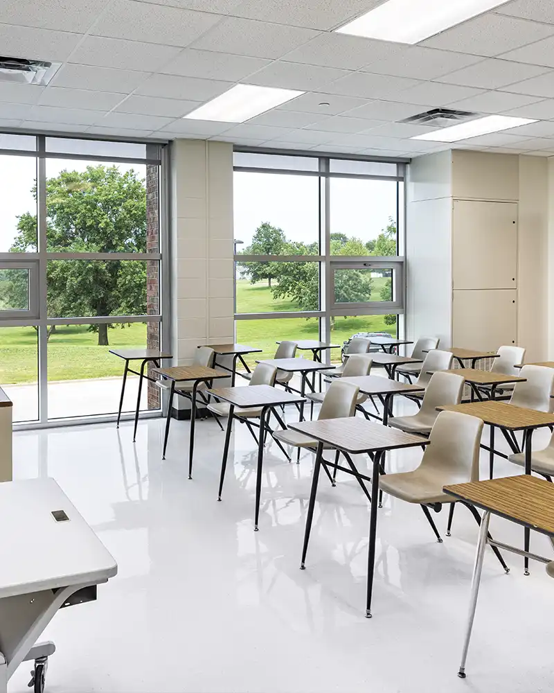 The interior of a classroom with large glass windows and desks in rows