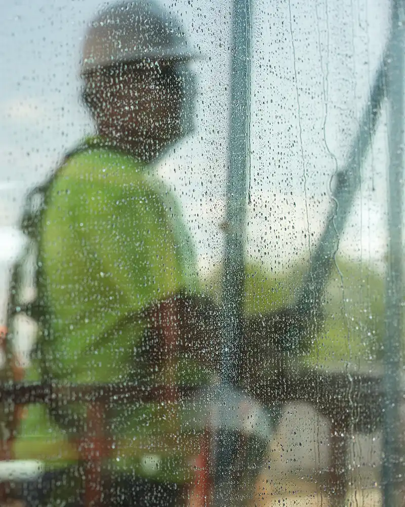 The reflection of a window washer worker appears on a wet window