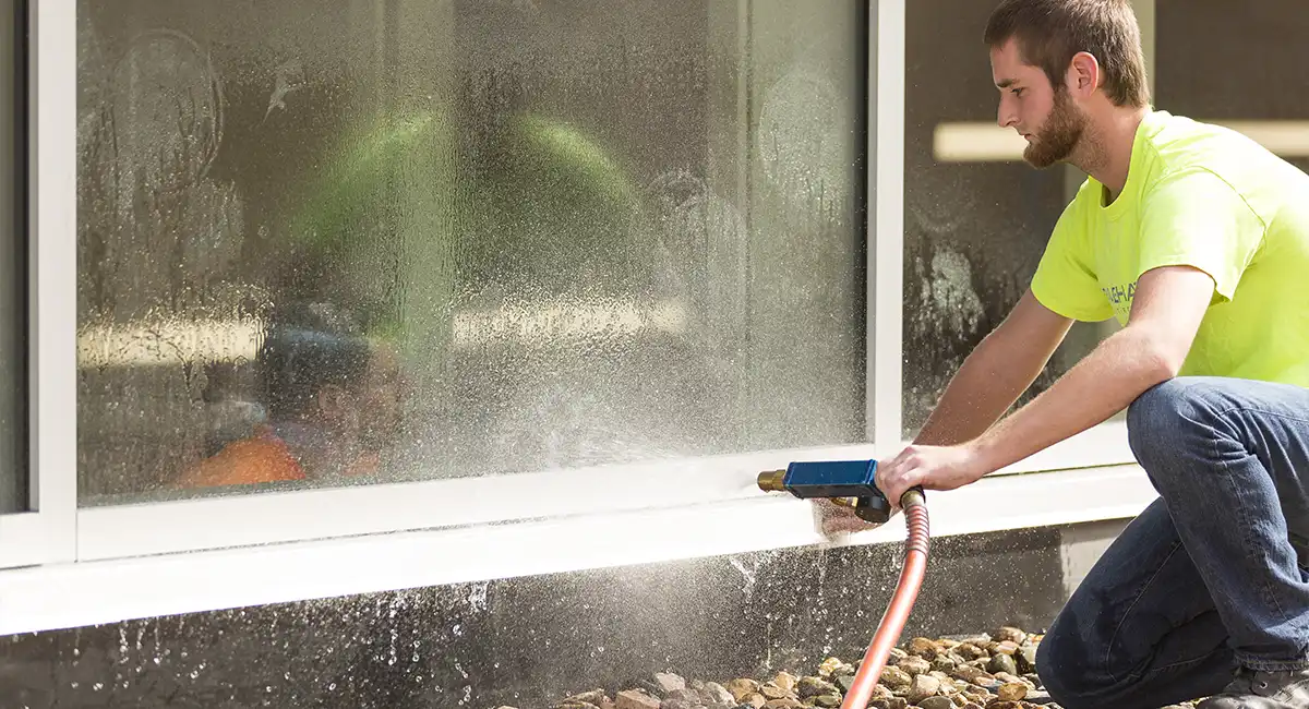 A young man sprays the outside of the glass on a building