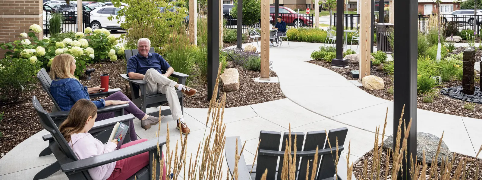 Three people sit under pergola among plantings