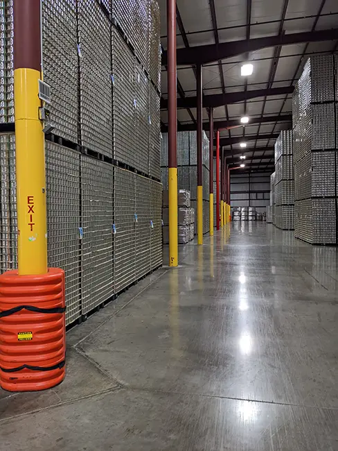 Interior of a warehouse with tall stacks of empty aluminum cans and bright yellow safety posts.