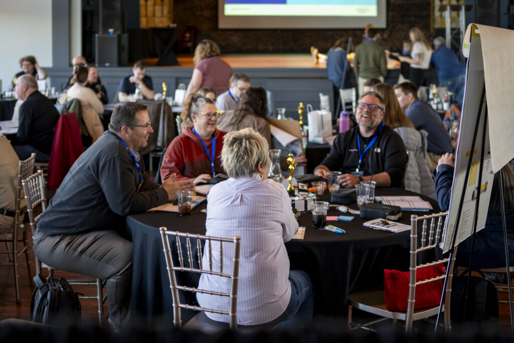 Corporate team members talking around a round table during small-group discussions at the 2026 Corporate Swarm